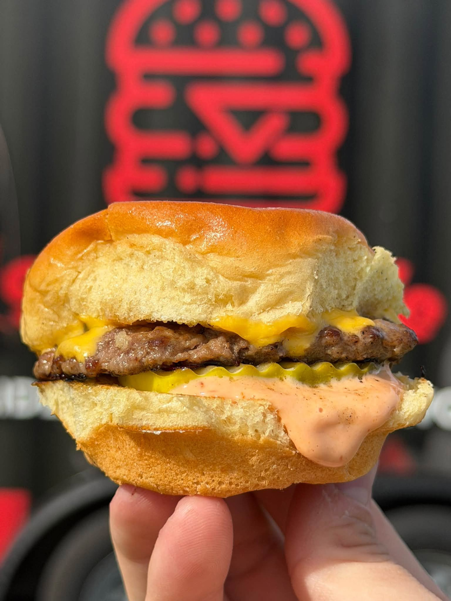 Slide Hustle cheeseburger slider stacked with pickles and sauce